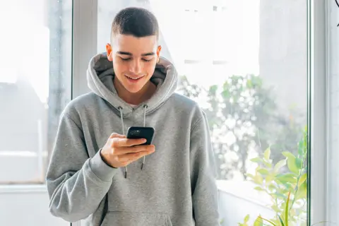 Junger Mann schaut lächelnd auf sein Smartphone