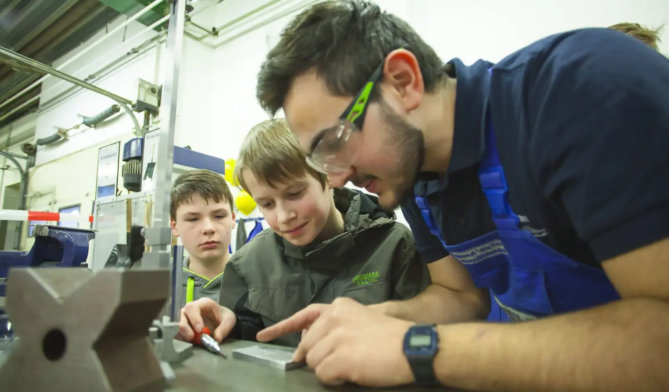 Abend derAusbildung bei der Meyer Werft: eine gewerbliche Fachkraft erklärt zwei Jungen technische Einzelheiten.